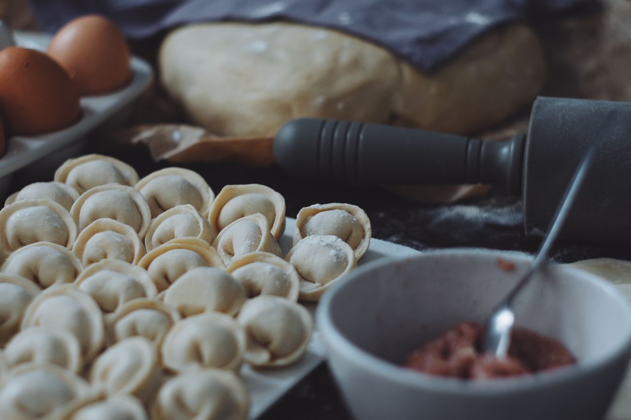 Close-up of uncooked dumplings with dough, eggs, and rolling pin for food preparation.