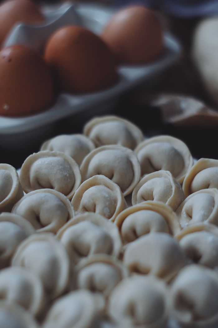 Detailed view of uncooked pelmeni on a kitchen surface with eggs in the background.