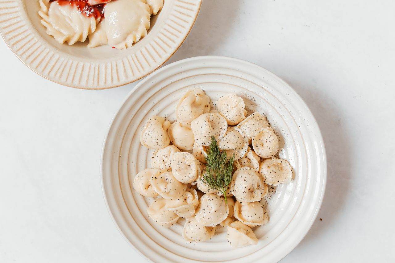 Close-up of Russian dumplings on ceramic plates garnished with dill, on a white surface.